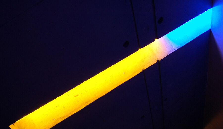 Long straight opening in concrete ceiling with bright coloured light emerging graduating from yellow to blue