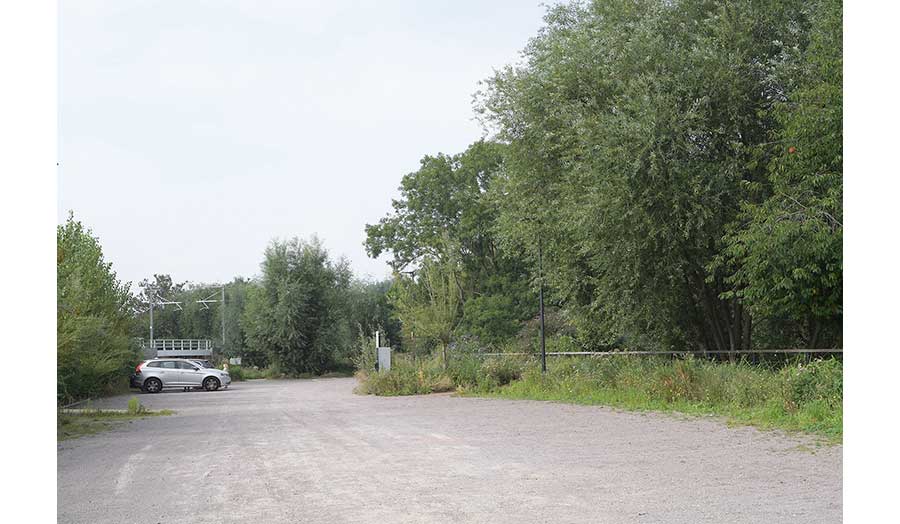 Silver car in carpark between railway line and trees