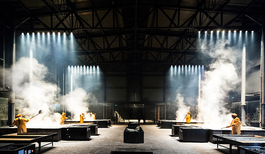 Tables in factory space, steam, lit from above. People in yellow uniforms