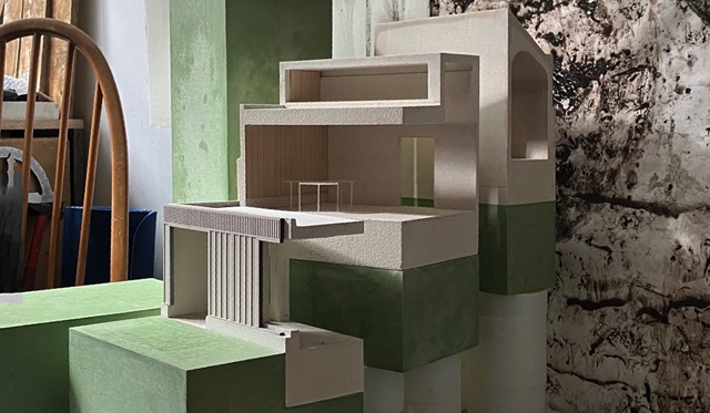 green and white sectional model of a building in a domestic setting with back of bentwood chair
