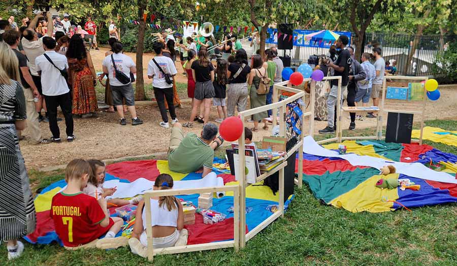 People on colourful mats inside a low wooden library structure, in an outdoor festival setting