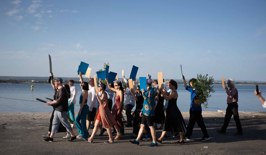 A choir walking through seaside town carrying colour and plants