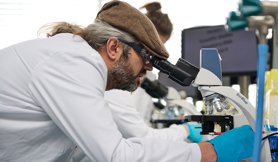 Man in flat cap with beard looking through a microscope in London Met's Superlab