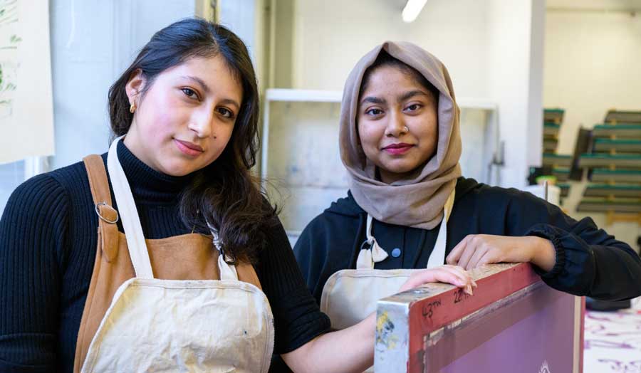 Two students smiling at the camera with textile work