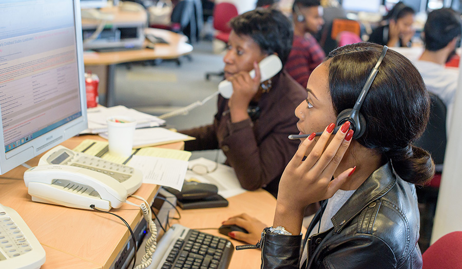 Photograph of call handlers with headsets sat in front of computers.