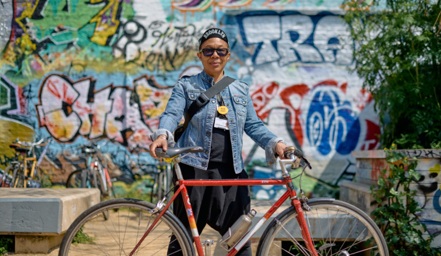 Staff member Donna Jones standing behind her red bicycle. The background is a wall full of graffiti.