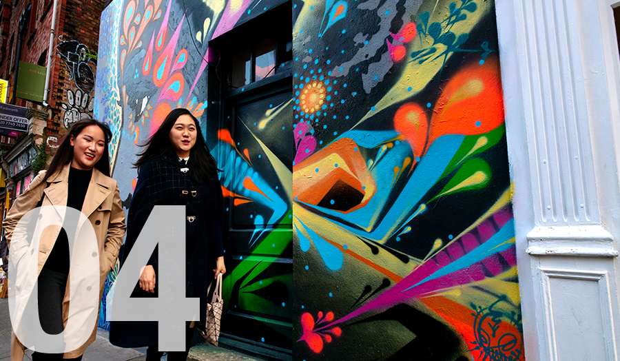 Two international students in Shoreditch walking past colourful graffiti