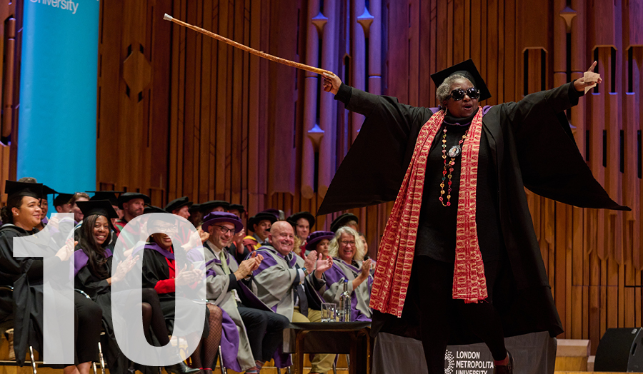 Older London Met graduate wearing dark glasses with walking stick in air in joy