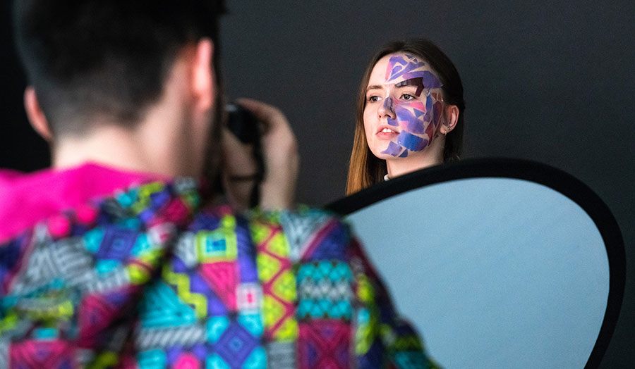 A London Met student with geometric makeup applied to half her face being photographed by another student