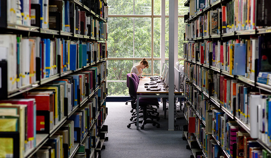 A student sitting at a desk between two rows of library books