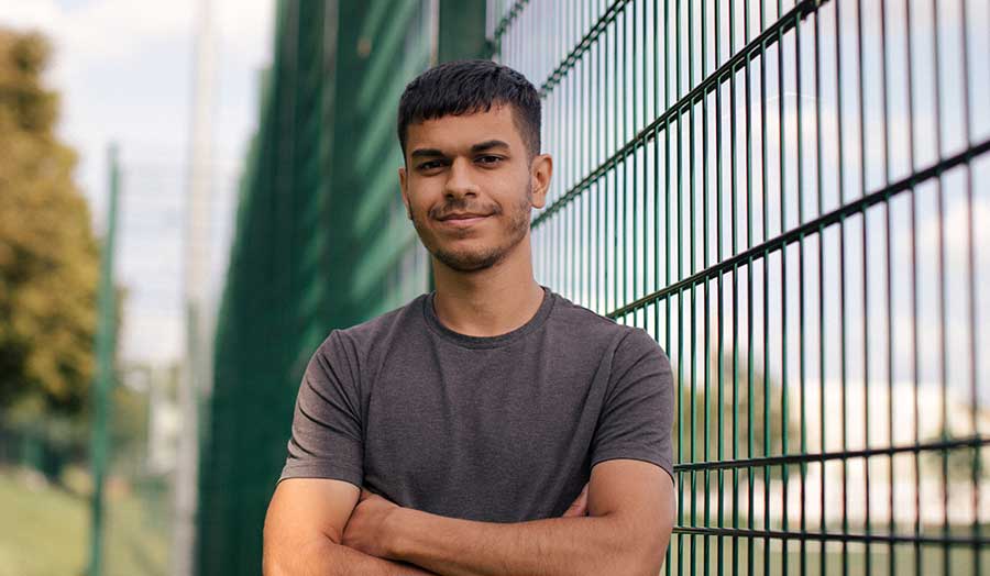 Aaron standing against a fence at a football pitch