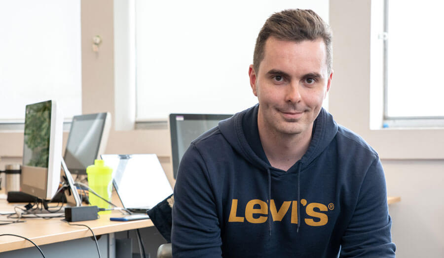 Short-haired male student Gyorgy Antal wears a long-sleeved t-shirt as he sits at a desk.