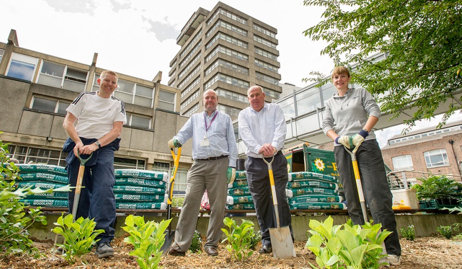 London Met staff pose with spades in Courtyard with tower building in background 