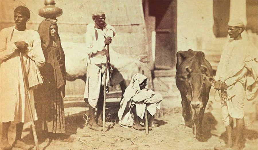 Sepia tone image of people in a village. There is a cow.