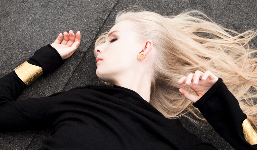 Blonde model lying down in black jumper with gold bangle and earring 