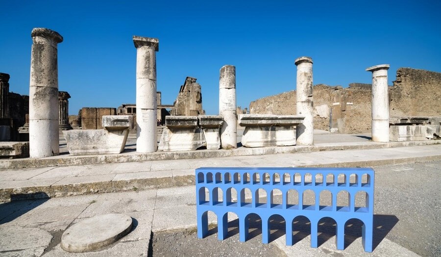 blue furniture shaped like an aqueduct photographed among real roman ruins