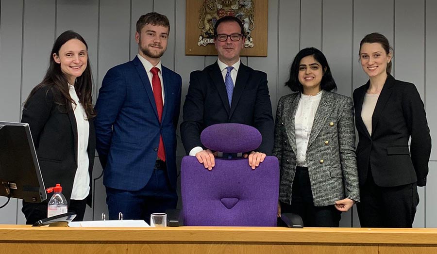 Paul and Alison stand with their opponents in a mock courtroom