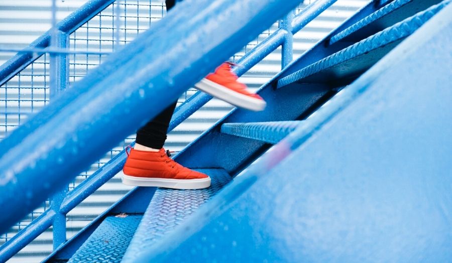 A person in red shoes walking up a set of blue stairs.
