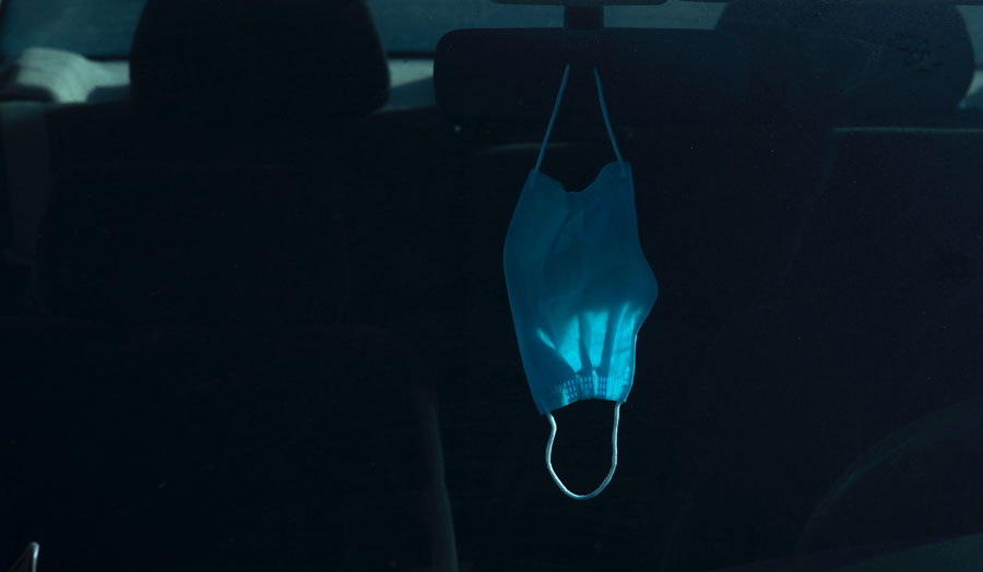 A medical mask hanging from a dashboard mirror