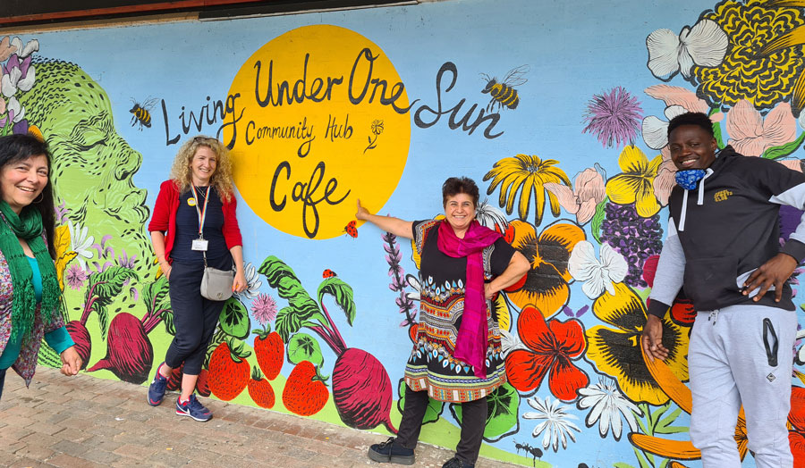 group of people standing in front of a mural which reads 'Living Under One Sun'