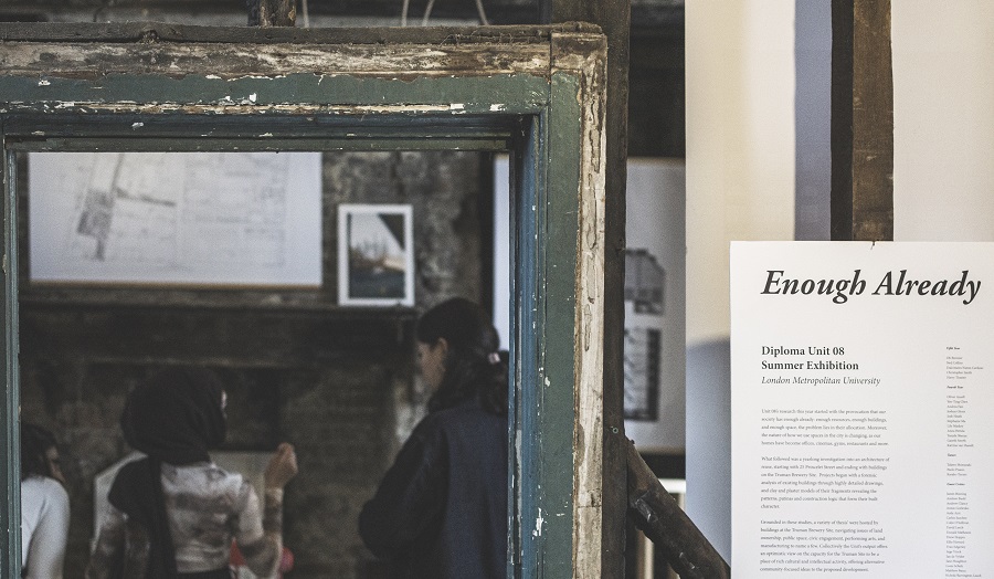 mirror with woman reflected in it next to gallery sign reading 'Enough Already'