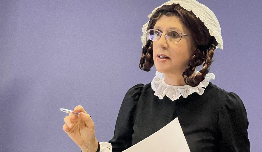 woman delivering lecture, wearing old fashioned bonnet and clothing to resemble Florence Nightingale