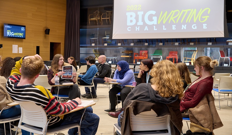 Students sat in a circle, discussing literature. Big Writing Challenge sign in background