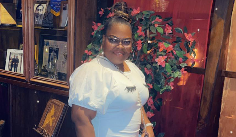 Sharon Foster posing in white dress in front of flowers