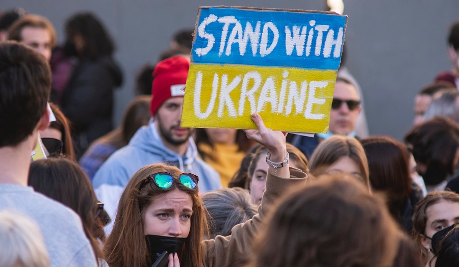 woman holding protest sign reading 'stand with Ukraine'.