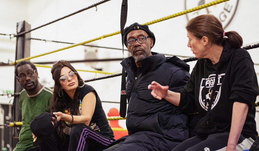 Actor Lenny Henry sitting on the side of a boxing ring with three other people.