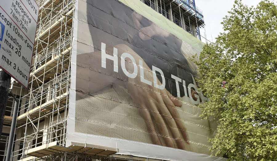 a hoarding covering a construction site, which shows two men embracing and the words 'hold tight'