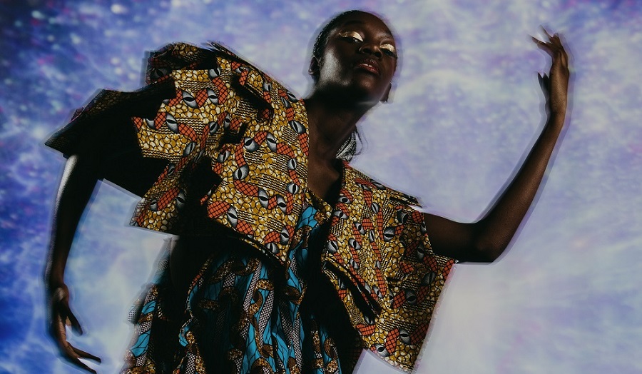 Woman wearing gold eyeshadow and colourful African Wax fabric clothing, against a blue background