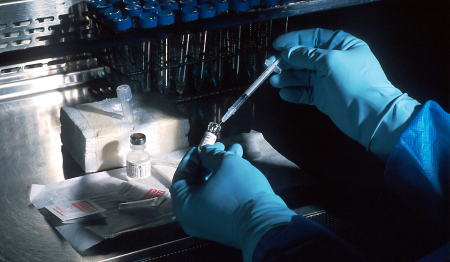 A scientist holding a needle and a bottle demonstrating biomedical science