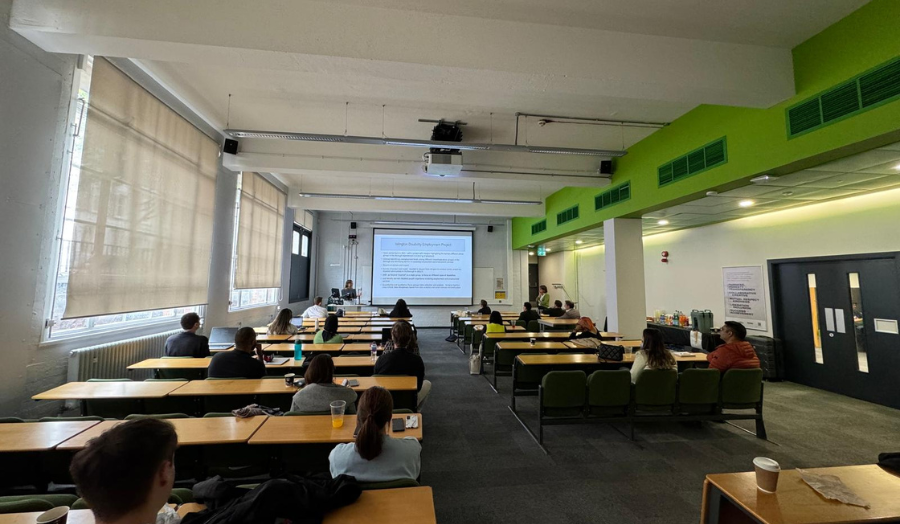 A large room filled with people with someone presenting at the front of the room