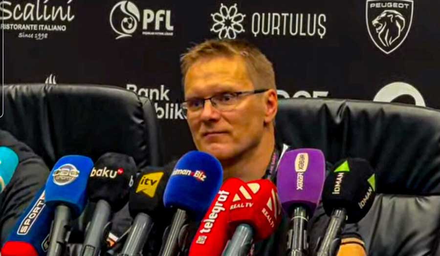 A football coach answers questions in front of a lot of microphones