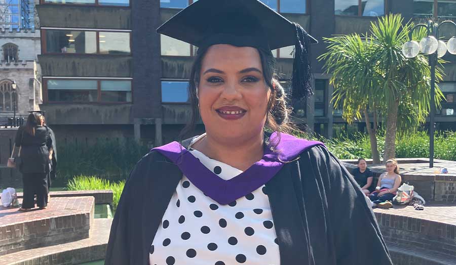 A woman wearing a cap and gown and white polkadot dress smiles 
