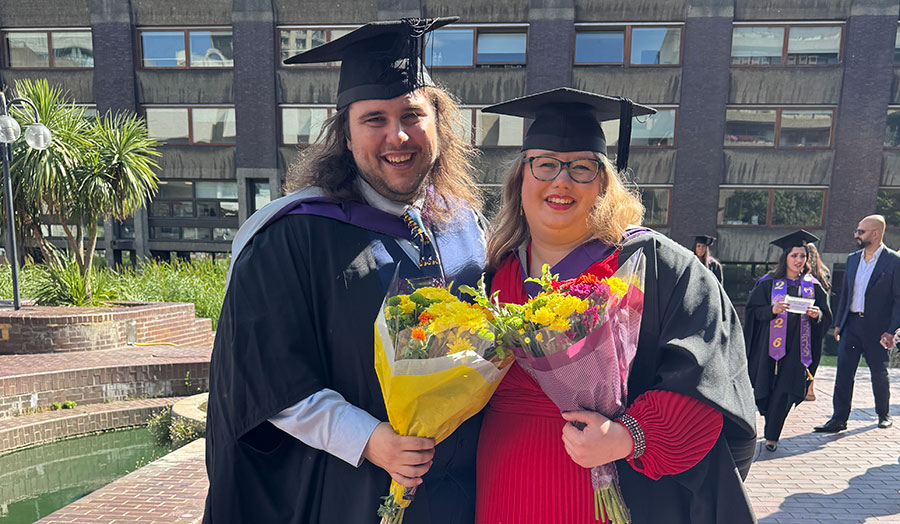 A man and a woman pose holding flowers in graduation robes and hats