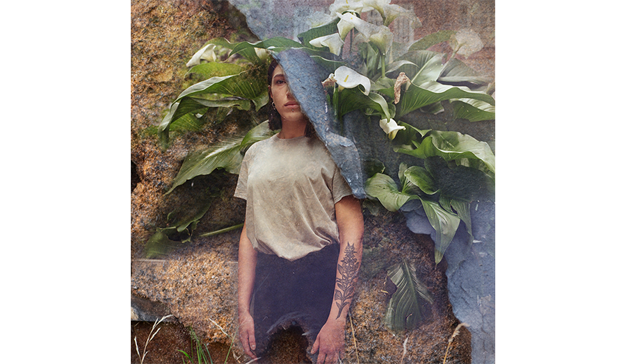 A person poses with a background of plants and a rock surface