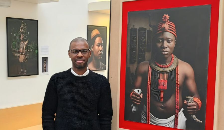A man stands in art exhibition with portraits behind him inspired by Nigerian sculptures