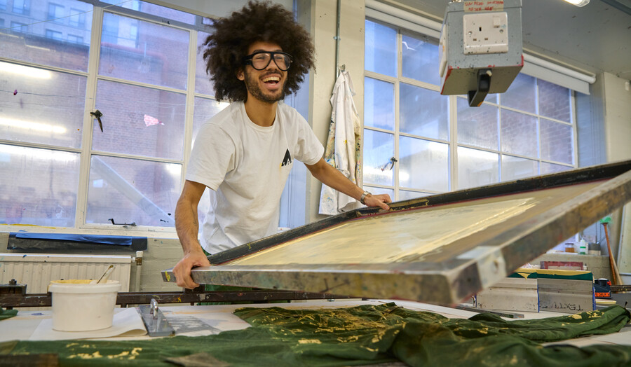 A student is laughing and wearing glasses while working on a textiles project