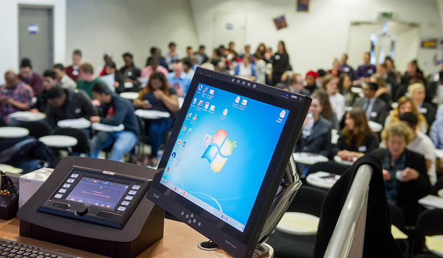 Image of a conference in progress, in the forefront is a computer.