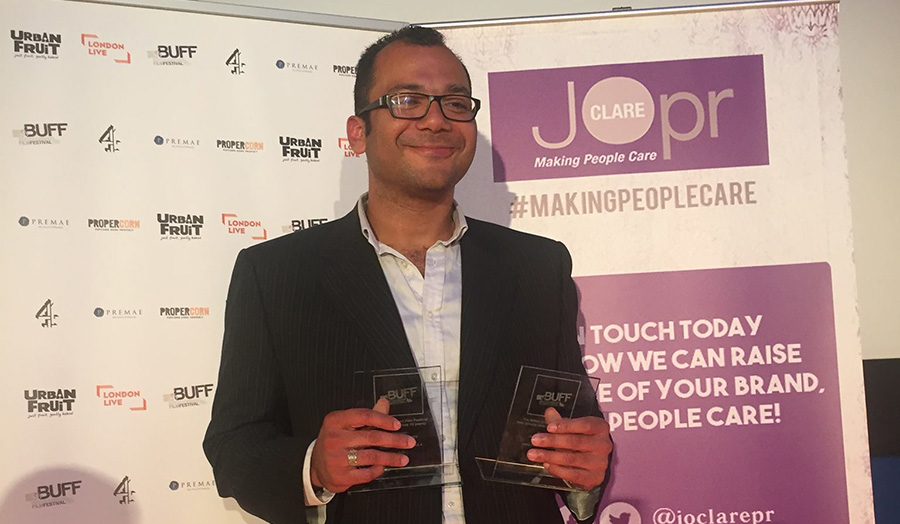 Jesse Quinones holds his two BUFF awards, smiling, in front of cameras