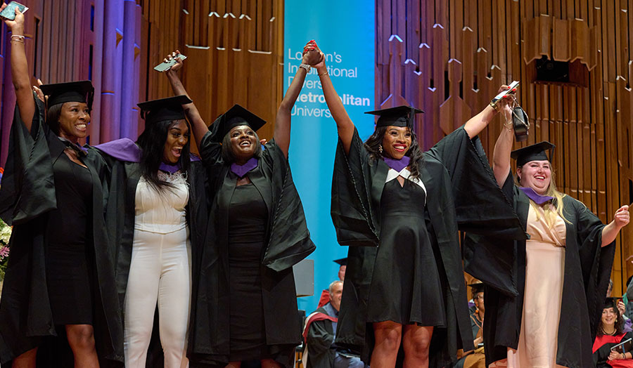Several London Met mature students at graduation holding hands and smiling on stage