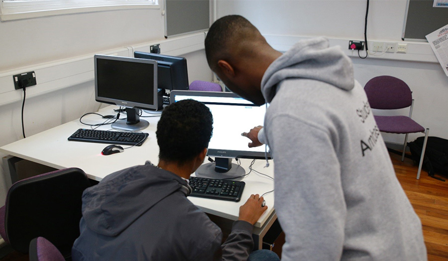 Mentoring with schools and colleges, male student helping another at a computer
