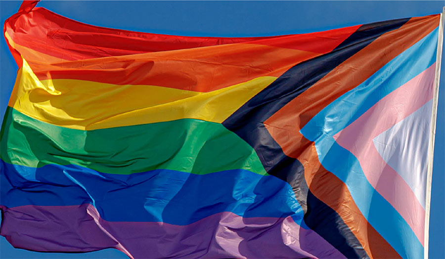 A LGBTQ+ flag on a pole and fluttering in the wind