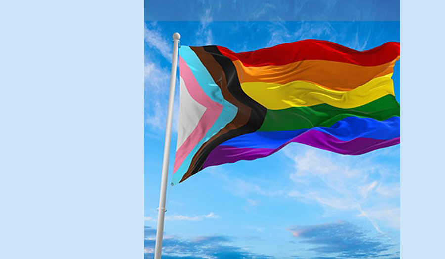 An LGBTQ+ flag on a pole and fluttering in the wind