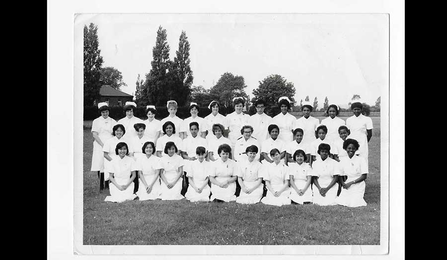 A black and white picture with nurses sitting outside arranged in three rows