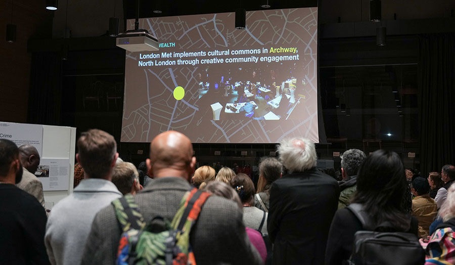 A crowd in a darkened room look at a PowerPoint presentation