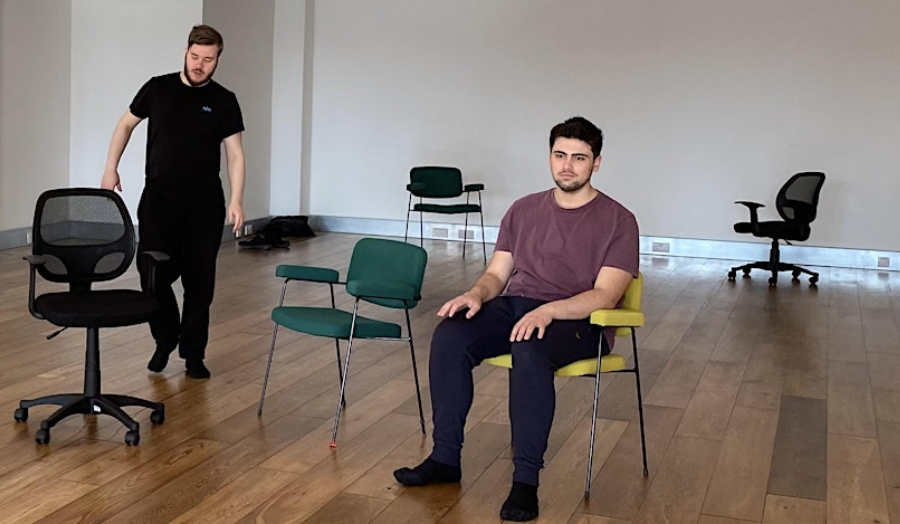 Two male participants taking part in the forum theatre workshops. One is seated, another is standing