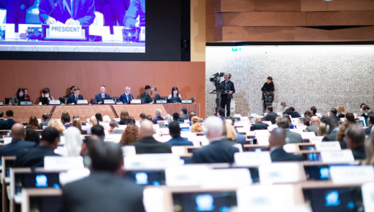 A panel of seven delegates at the United Nations sit in front of an audience